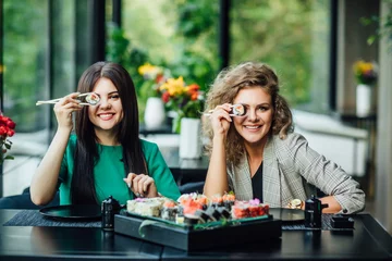  Lunch at a Chinese restaurant on the summer terrace. Two sistres  eat sushi with chinese sticks. © Тарас Нагирняк