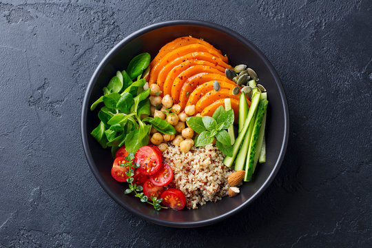 Healthy vegetarian salad. Roasted pumpkin, quinoa, tomatoes, green salad. Buddha bowl. Slate background. Top view.
