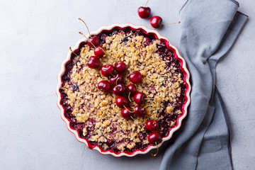 Cherry, red berry crumble in baking dish. Grey stone background. Top view.