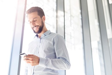 Fototapeta premium Businessman smiling while using smartphone in office
