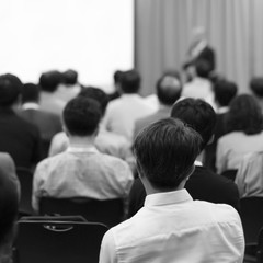 Speaker on the stage with rear view of audience in the conference hall or seminar meeting, business and education concept. Speaker giving a talk at business meeting. Seminar presentation photo.