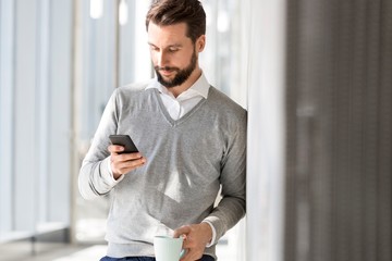 Businessman standing leaning on wall while using smartphone