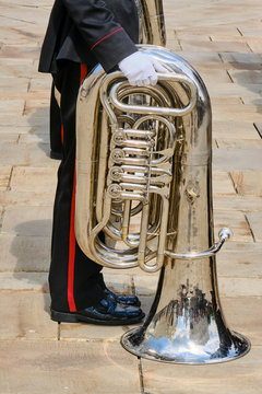 A military musician stands with a tuba on the stone parade ground