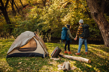 Young beautiful couple with hiking backpacks go trekking. Attractive woman and handsome man relaxing together in nature near tent.
