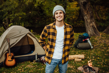 Portrait of young male tourist standing in the forest with tent.