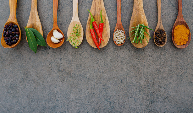 Various of spices and herbs in wooden spoons. Flat lay spices ingredients chili ,peppercorn, rosemary, thyme on dark stone background.