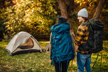 Young beautiful couple with hiking backpacks go trekking. Attractive woman and handsome man relaxing together in nature near tent.