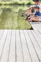 Father and son sitting on pier while fishing in lake