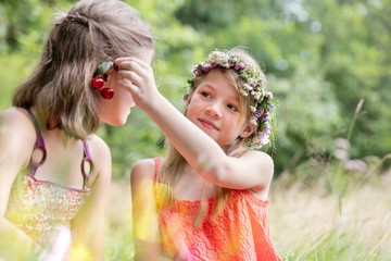 Obraz premium Cute girl holding cherry fruits on friend's ear at park
