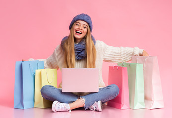 Carefree winter girl with laptop sitting with shopping bags