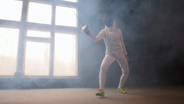 A young woman fencer in white protective costume performing basic attack movements