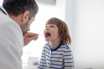 Pediatrician checking child patient's tonsil in clinic