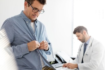Patient undressing while doctor writing report in clinic