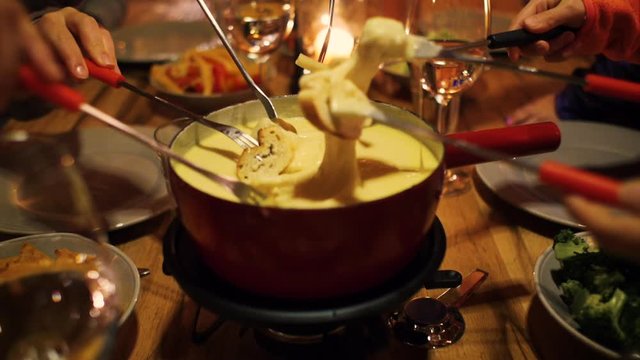 a family enjoying cheese fondue and they stick bread in the melted cheese in a cabin lodge setting