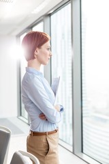 Young thoughtful businesswoman looking through the window in office