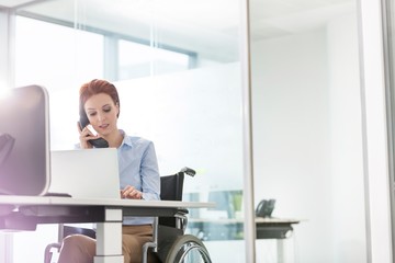 Businesswoman sitting on wheel chair while working in office