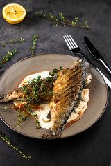 fried rainbow trout fish with lemon sauce and thyme on black marble table as background
