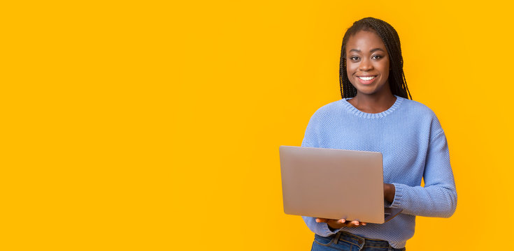 Cheerful black girl holding laptop over yellow background