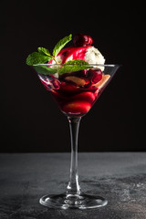 Dessert with Cherry Sauce, biscuits and mint in a martini glass on a grey table and black background