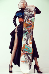 Professional top model posing with a snowboard. Concept of winter sports. Stylish dress and high heels.