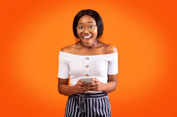 Excited Afro Girl Using Mobile Phone Smiling Standing, Orange Background