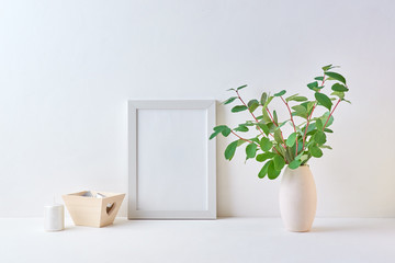 Mockup with a white frame and branches with green leaves in a vase on a light background