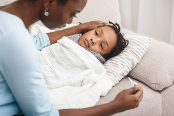 Mother measuring temperature of her sick daughter