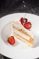 a piece of delicate cake, with slices of sliced strawberries, with the effect of powdered sugar, on a white plate on a white and gray background
