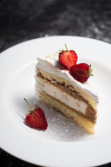 cake, a piece of delicate cake, with sliced fresh strawberries, on a white plate, on a white and gray abstract dark background. confectionery