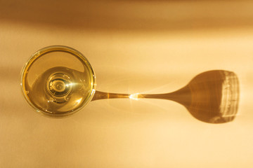 Glass of champagne on a light background. An impressive long shadow falls from the glass. The original concept of the holiday, alcoholic drinks. Minimalism, top view.