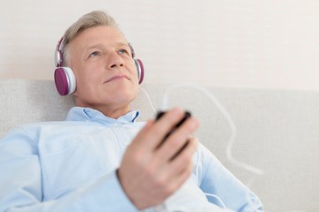 Mature man relaxing while listening music in bedroom at home