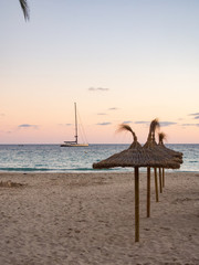 Sunset on the beach with straw umbrellas in Mallorca, Spain