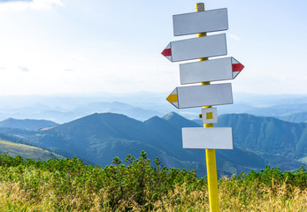 Blank signpost on a sunny day with mountains, beautiful blue sky and clouds.