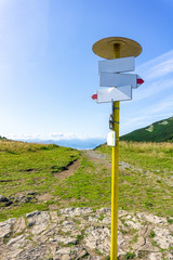 Blank signpost on a sunny day with a road in the mountains, beautiful blue sky and clouds.