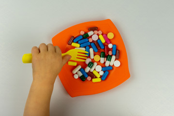 The child 's hand is  with a toy fork  trying to eat pills. The concept of dangerous pill use by children.