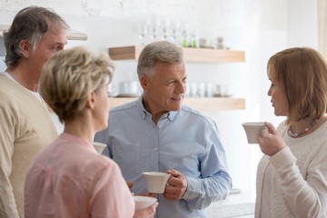 Fototapeta premium Mature friends holding drinks while talking in living room at home