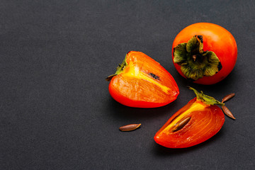Ripe single persimmon. Fresh whole fruit, half sliced, seeds. Isolated on matte black background