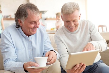 Smiling mature men using digital tablet while sitting on sofa at home