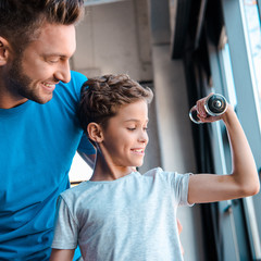 handsome father looking at cheerful son exercising with dumbbell