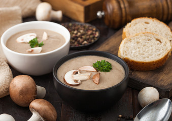 Ceramic bowl plates of creamy chestnut champignon mushroom soup with spoon, pepper and kitchen cloth on dark wooden  background and fresh bread.