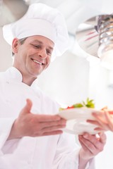 Smiling chef giving salad plate to waiter in kitchen at restaurant