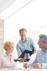 Young waiter showing menu to mature couple at restaurant