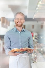 Portrait of smiling young waiter holding fresh bread in tray at restaurant