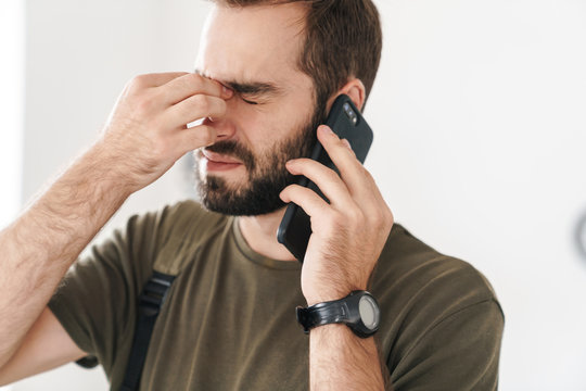 Image of caucasian tired man with headache talking on cellphone