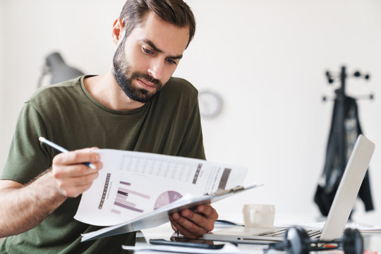 Image of thinking handsome man reading documents and holding clipboard