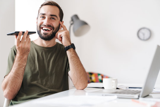 Image of handsome excited man talking on cellphone and using laptop