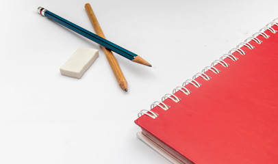 2 pencils, an eraser and a red notebook placed on a white background