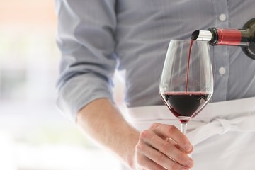 Midsection of waiter pouring red wine in wineglass at restaurant