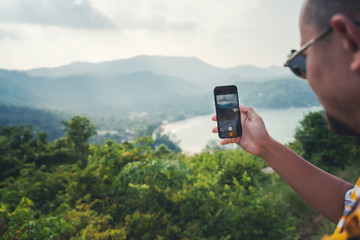 A male traveler takes a landscape on a cell phone point while traveling. Sea and mountain viewpoint