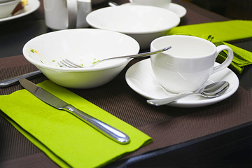Used cutlery on the table. Coffee cup, plate, knife and spoons on the table. Selective focus